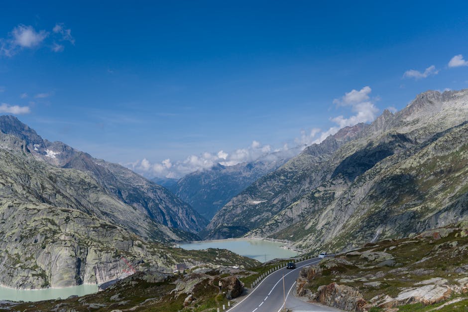 Breathtaking view of a road winding through the Swiss Alps, showcasing rugged mountains and a serene lake.
