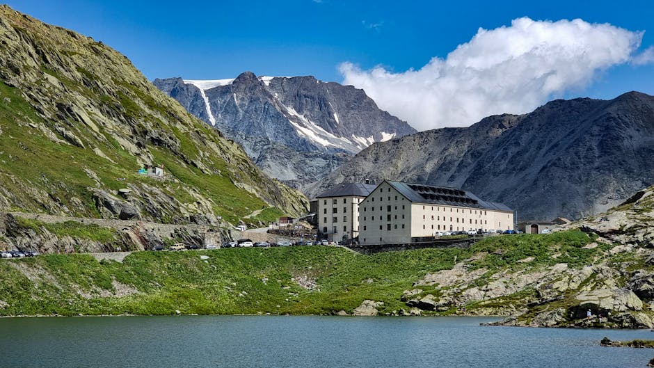 Picturesque landscape of Great St Bernard Pass with mountains and a historical building under a vibrant blue sky.