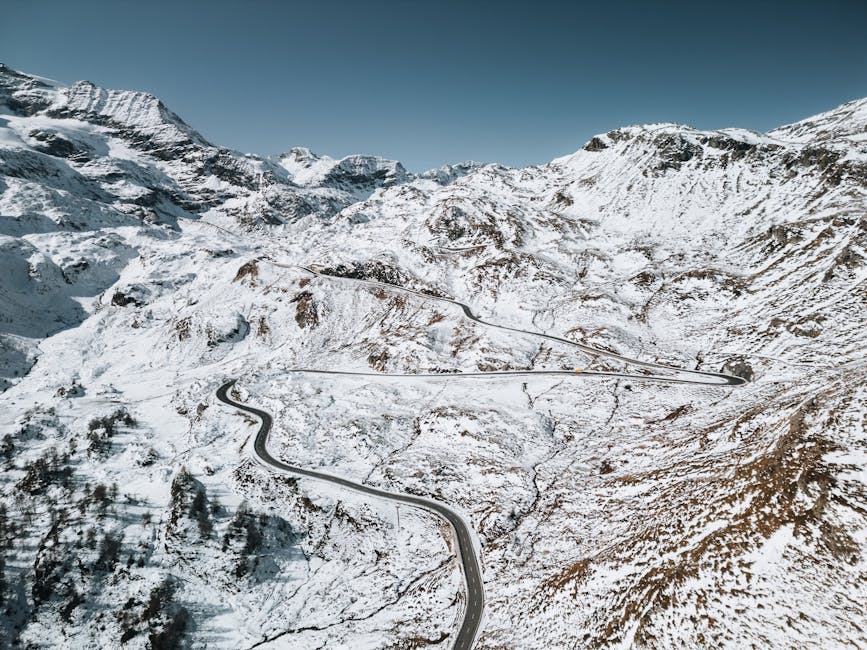 Aerial view of a winding road through snow-covered mountains, showcasing the stunning winter landscape.